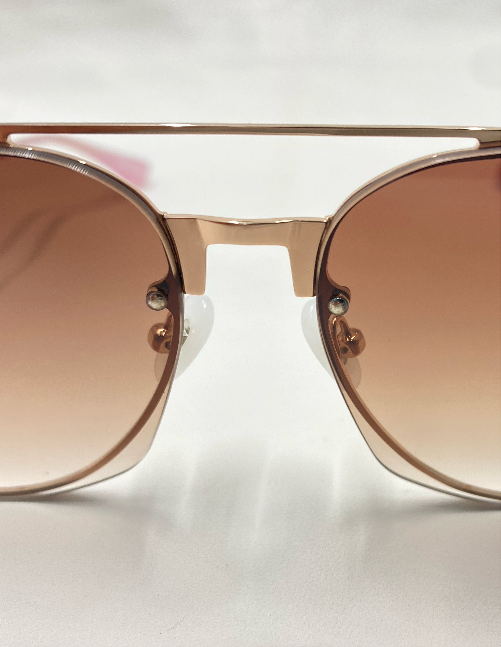 Close-up of brown-tinted For Art&#39;s Sake® Casino sunglasses with a gold-toned frame and a double bridge design. Featuring jadestone nose pads and 100% UV protection, the white background accentuates their sleek and modern style.