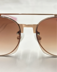 Close-up of brown-tinted For Art's Sake® Casino sunglasses with a gold-toned frame and a double bridge design. Featuring jadestone nose pads and 100% UV protection, the white background accentuates their sleek and modern style.