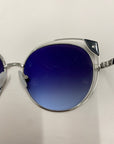 Close-up of Skylar, a pair of stylish sunglasses by For Art's Sake®, featuring silver metal frames and large, round lenses with a blue gradient tint. The UVA UVB-protected sunglasses are resting on a white surface, showcasing the hinge connecting the lens to the arm on the right side of the image.