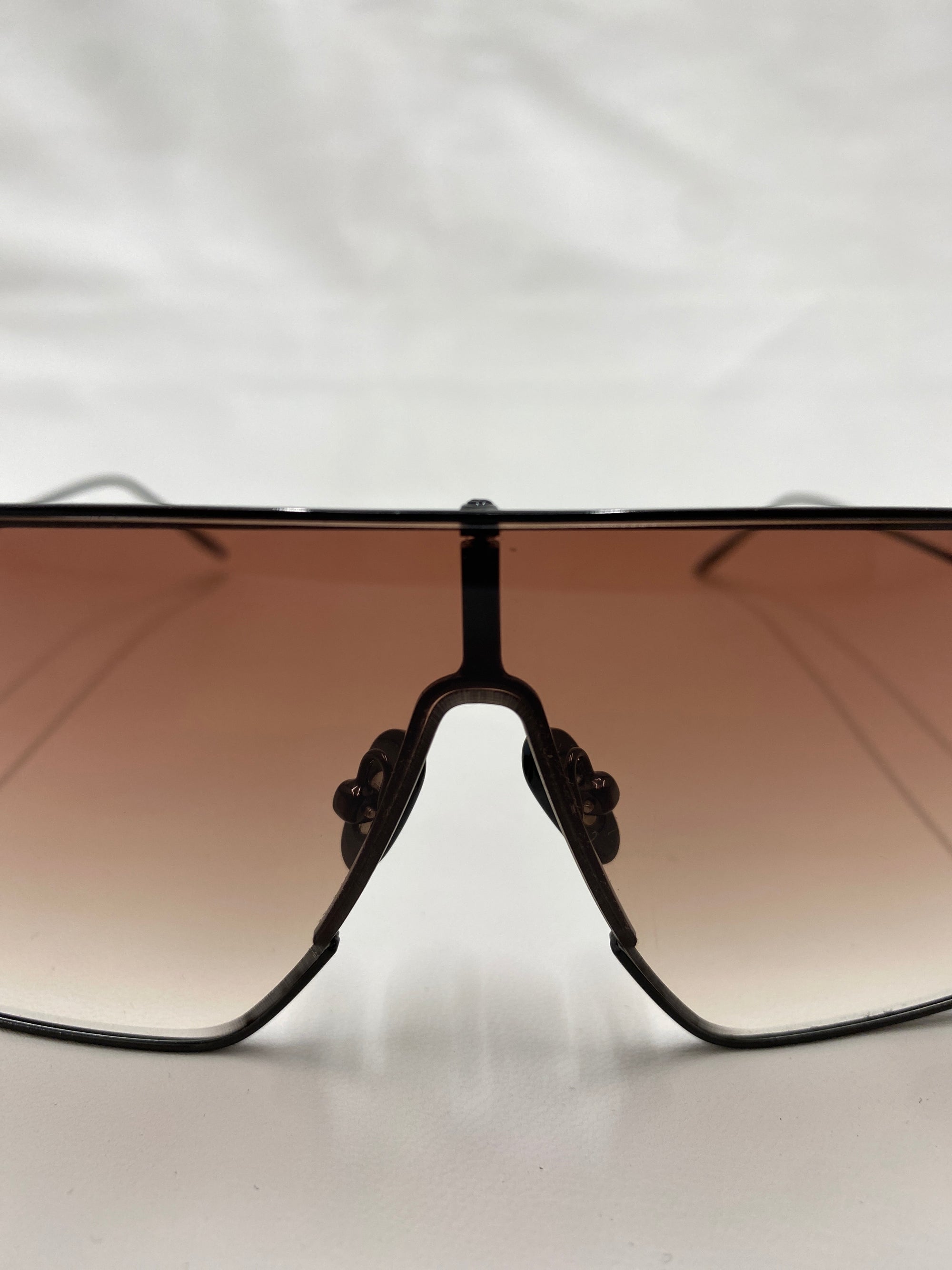 A close-up image of the front view of sporty, oversized For Art&#39;s Sake® Horizon shield sunglasses with dark brown gradient lenses. The thin black frame features jadestone nosepads for added comfort, all set against a clean white background. Enjoy 100% UVA &amp; UVB protection with these stylish shades.