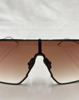 A close-up image of the front view of sporty, oversized For Art's Sake® Horizon shield sunglasses with dark brown gradient lenses. The thin black frame features jadestone nosepads for added comfort, all set against a clean white background. Enjoy 100% UVA & UVB protection with these stylish shades.