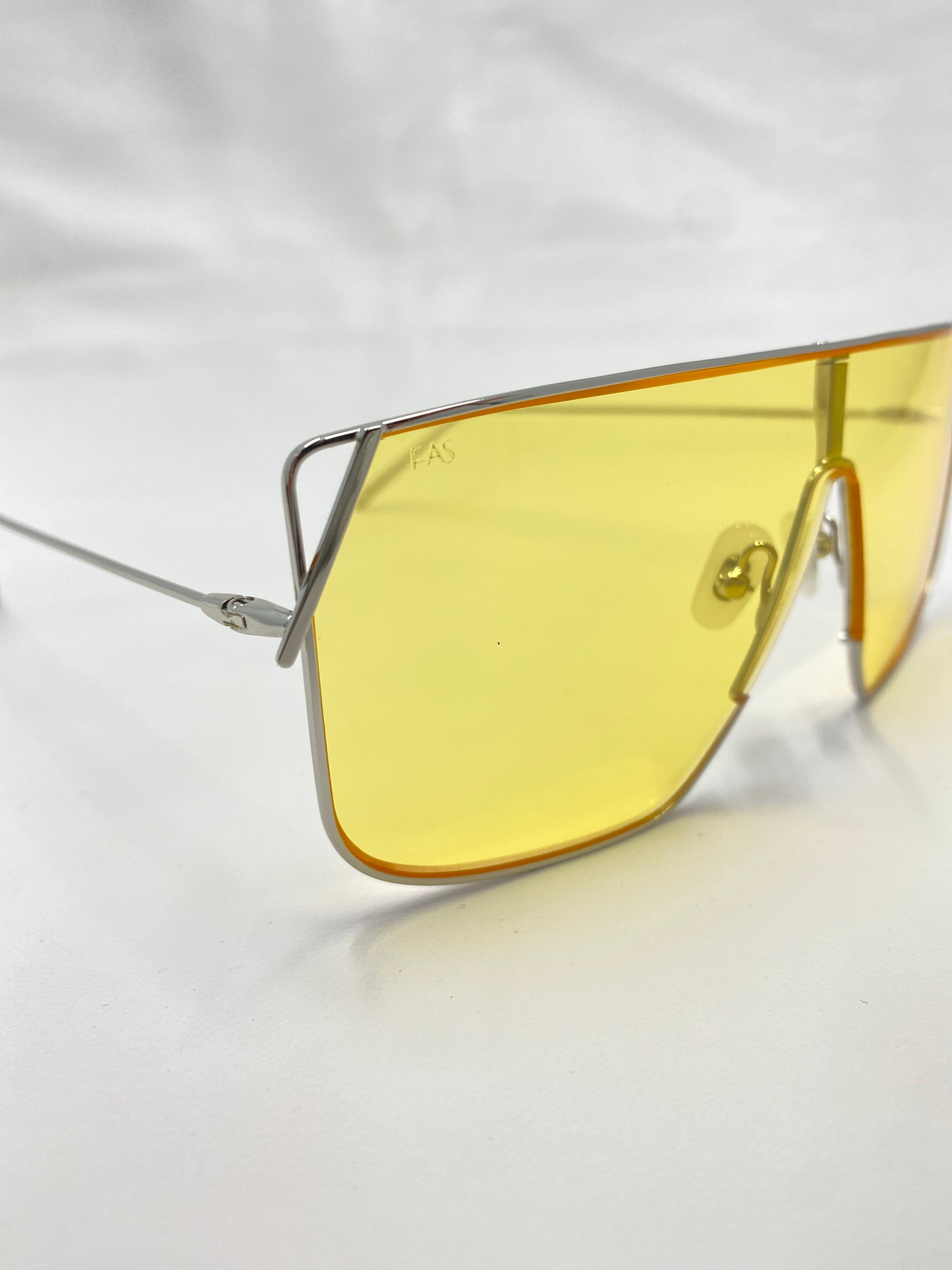 A close-up of the Horizon sunglasses by For Art&#39;s Sake®, featuring modern yellow-tinted nylon lenses and thin stainless steel frames. These sunglasses, offering UVA &amp; UVB protection, are set against a plain white background, highlighting their sleek and minimalist design.