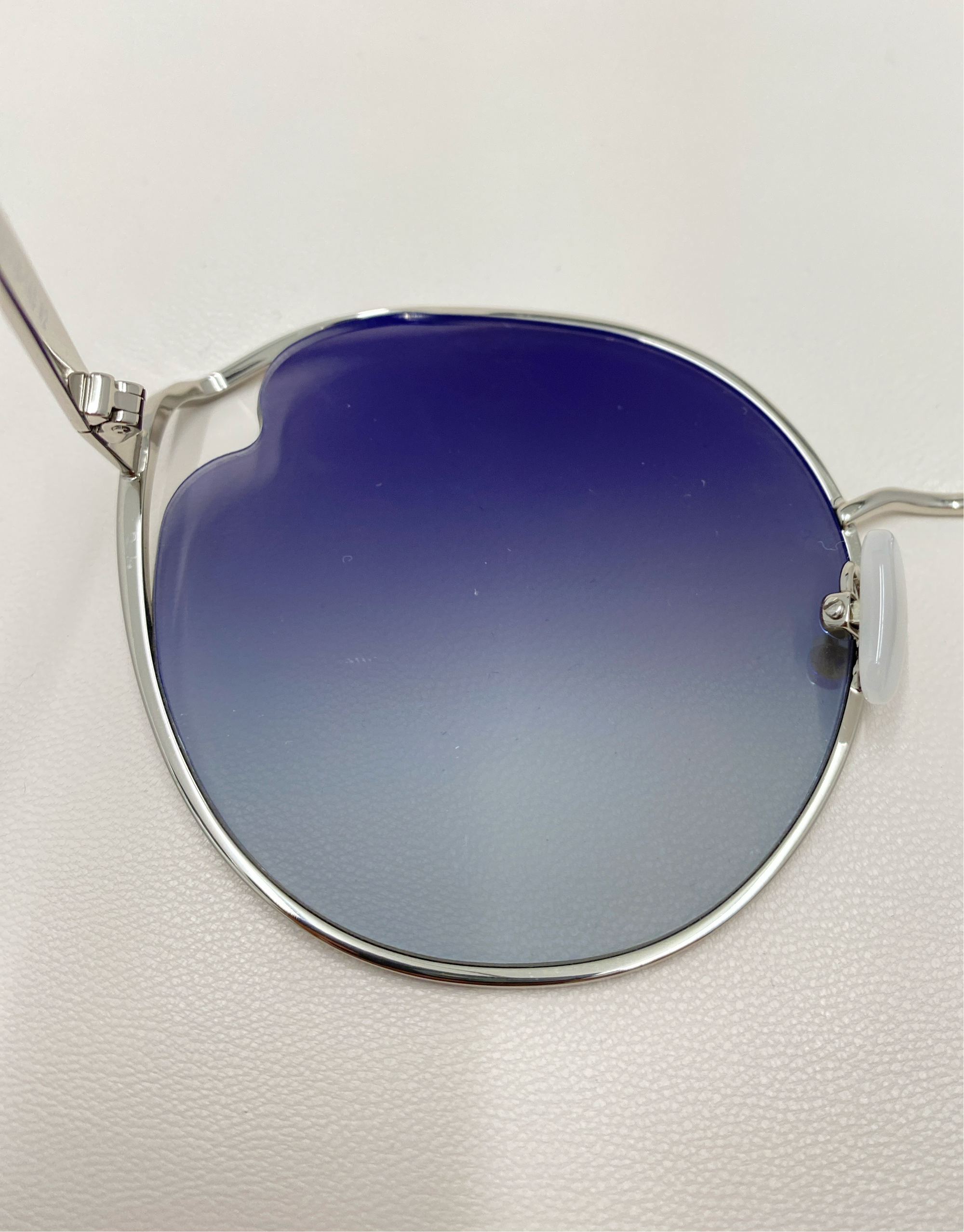 Close-up image of the Cat sunglasses by For Art&#39;s Sake®, featuring stylish thin silver frames and gradient blue to white, UVA &amp; UVB-protected nylon lenses, placed on a white surface. The photo highlights the elegant design, color transition of the lenses, and adjustable nosepads for added comfort.