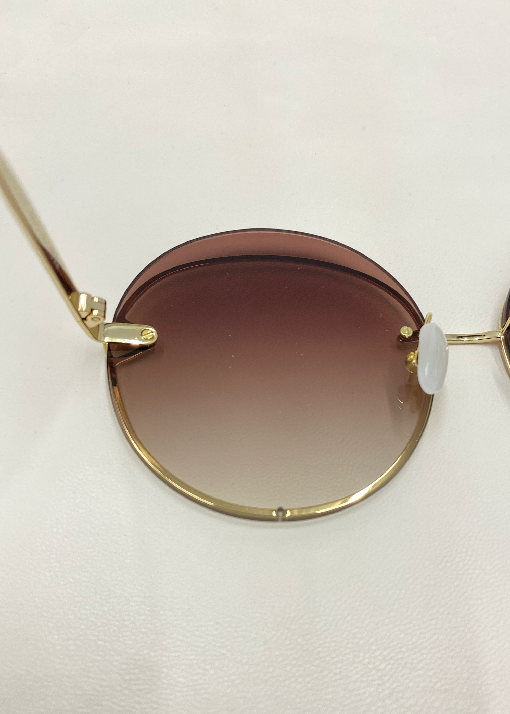 A close-up image of the Quartz sunglasses by For Art&#39;s Sake®, featuring 18-karat gold-plated frames and gradient lenses that transition from dark brown at the top to a lighter shade at the bottom. The Quartz sunglasses are lying on a white surface.