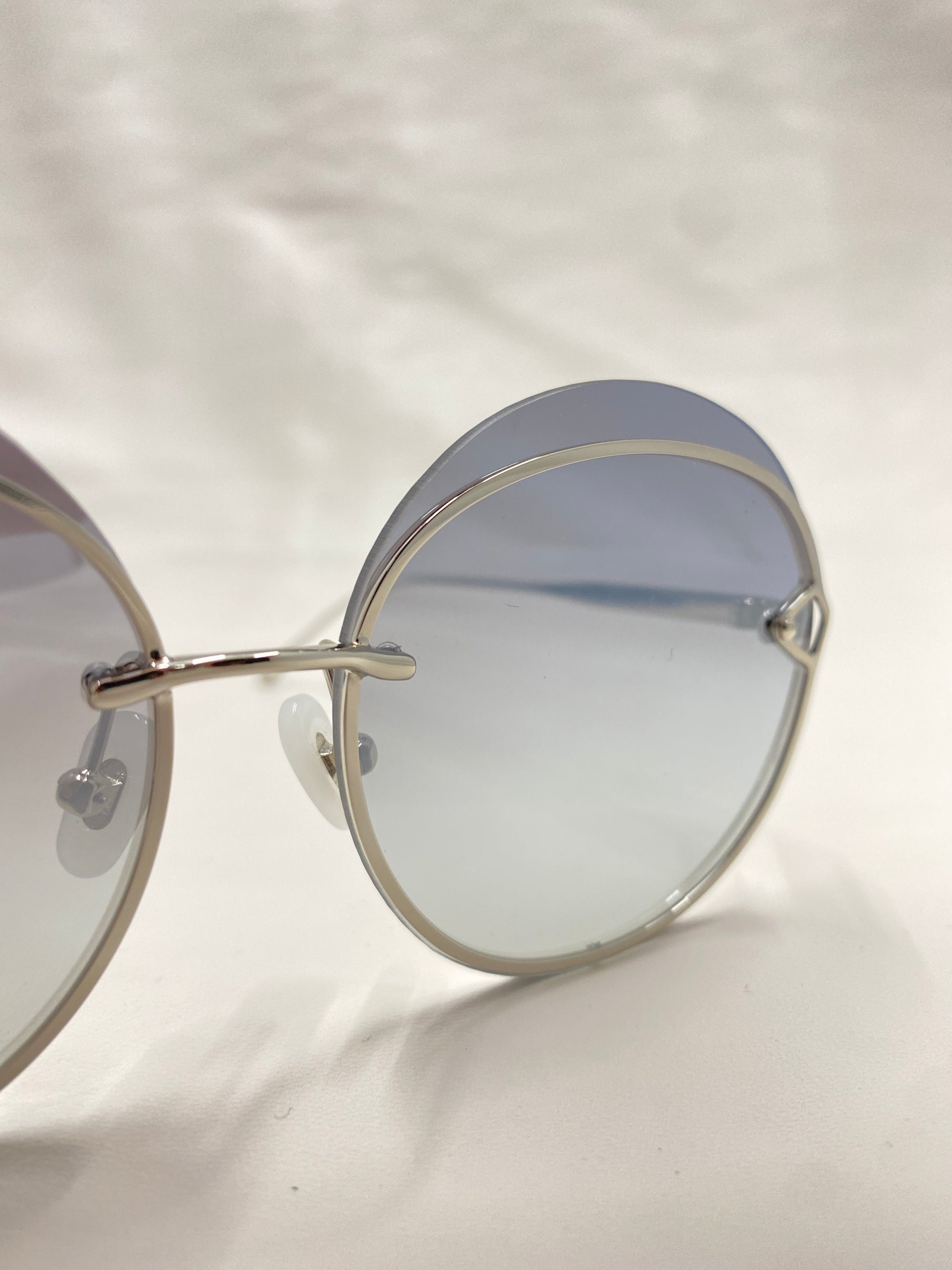 A pair of Quartz sunglasses by For Art's Sake®, featuring sleek stainless steel frames, adjustable nose pads, and lightly tinted round lenses. They are positioned at an angle, showcasing the stylish design and reflective nylon lenses against a plain, soft light background.