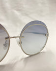 A pair of Quartz sunglasses by For Art's Sake®, featuring sleek stainless steel frames, adjustable nose pads, and lightly tinted round lenses. They are positioned at an angle, showcasing the stylish design and reflective nylon lenses against a plain, soft light background.