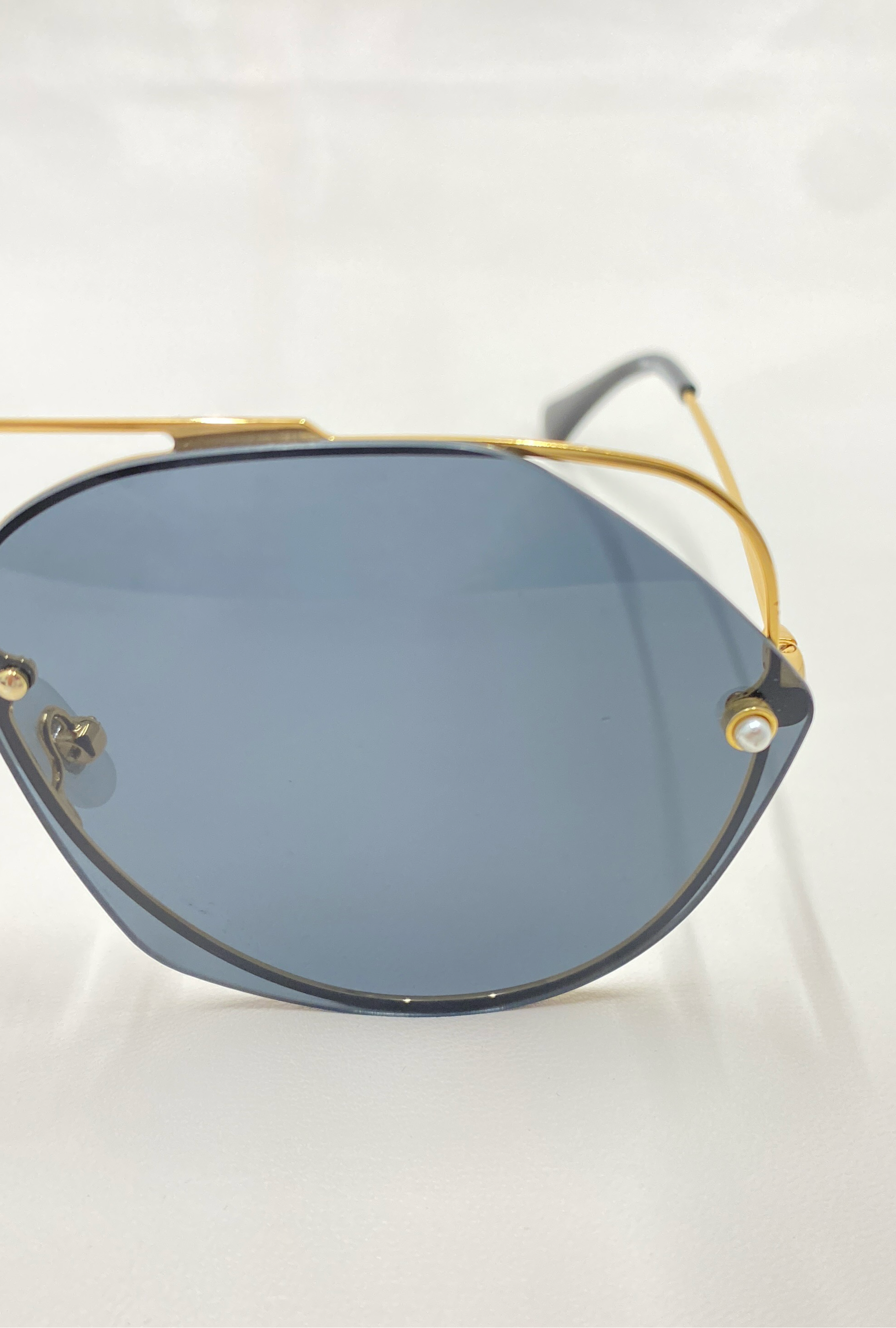 A close-up image showcases a pair of For Art&#39;s Sake® Casino sunglasses, featuring blue-tinted lenses and a gold-toned stainless steel frame. The sleek, modern design is highlighted by delicate, thin temples and visible nose pads. Experience UV protection on the go against the clean, white background.