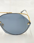 A close-up image showcases a pair of For Art's Sake® Casino sunglasses, featuring blue-tinted lenses and a gold-toned stainless steel frame. The sleek, modern design is highlighted by delicate, thin temples and visible nose pads. Experience UV protection on the go against the clean, white background.