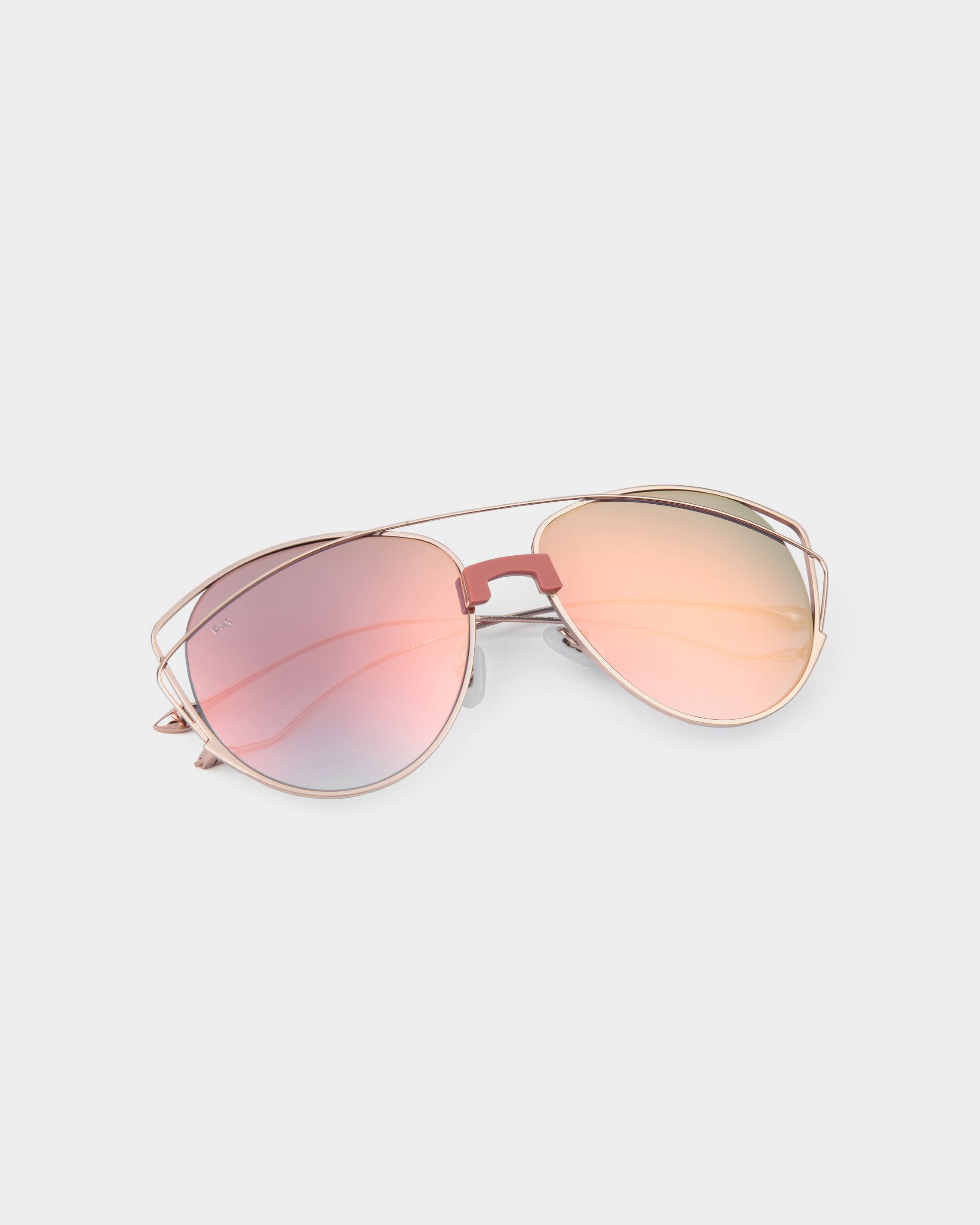 A pair of aviator-style sunglasses with stainless steel frames and pink and orange gradient nylon lenses, offering 100% UV protection, laid on a light gray background. The product name is Dark Eyes by For Art&#39;s Sake®.