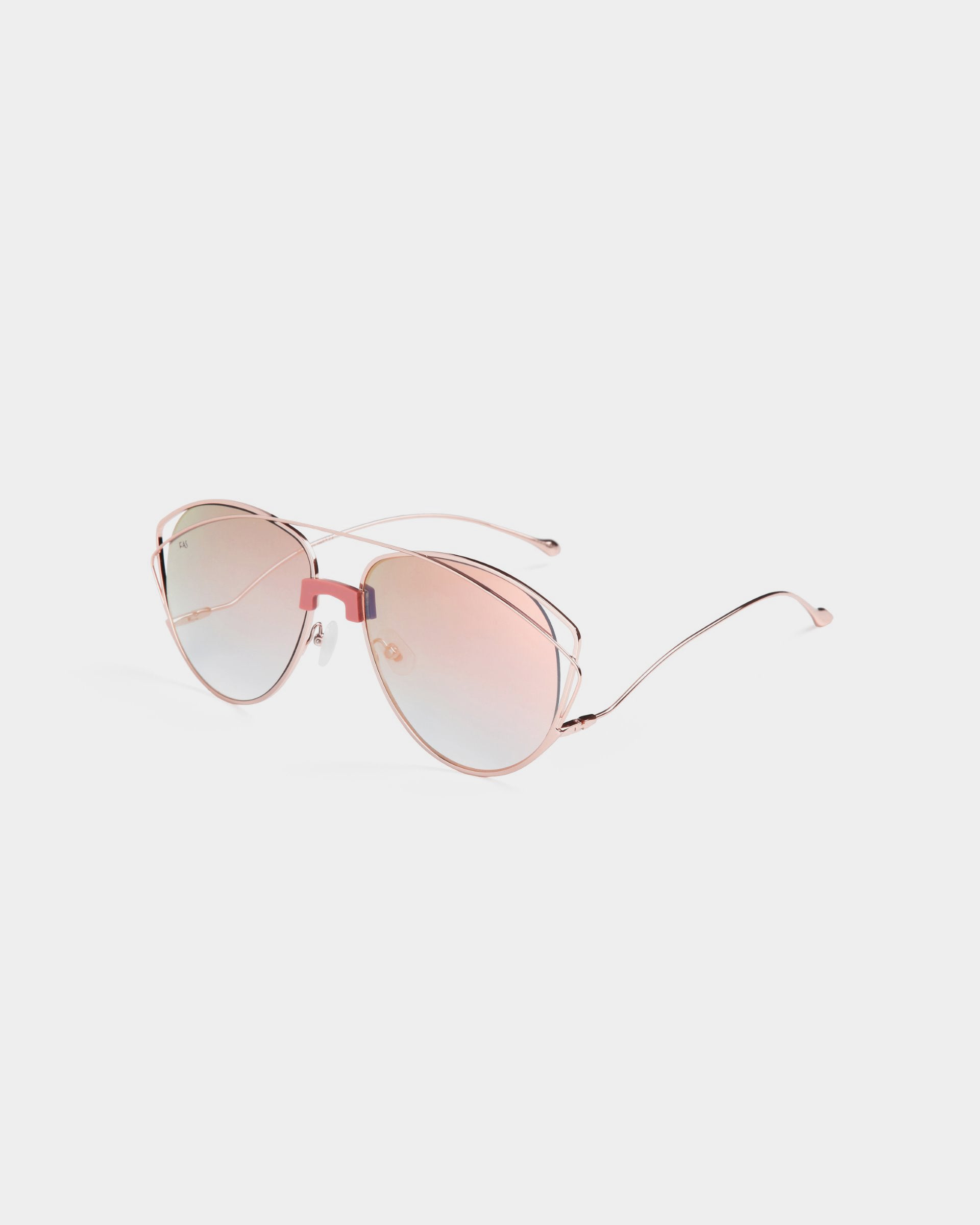 A pair of For Art&#39;s Sake® Dark Eyes aviator-style sunglasses with light pink-tinted lenses and rose gold stainless steel frames. The sunglasses have a sleek, minimalist design and thin arms, offering 100% UV protection while resting on a white background.