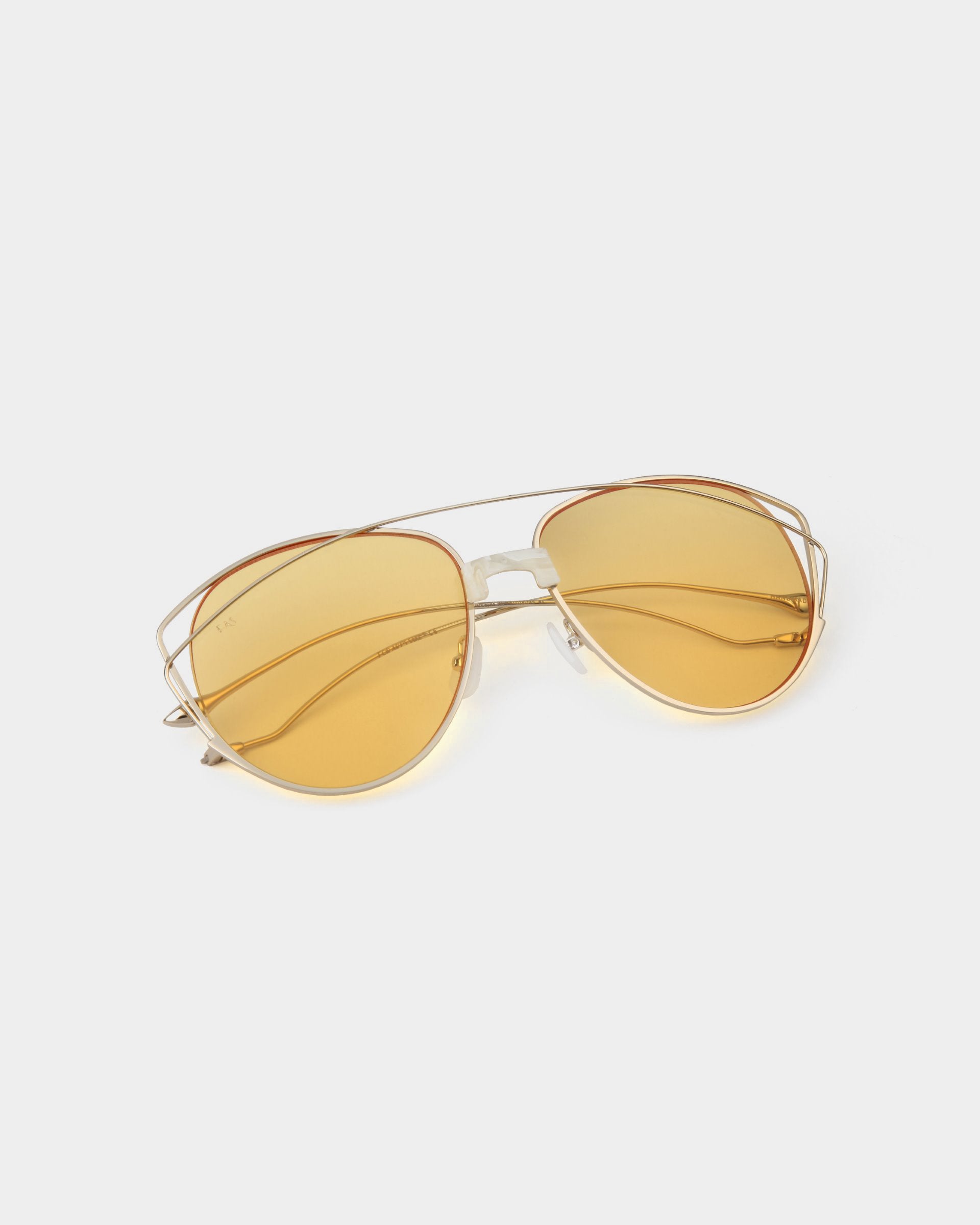 A pair of aviator-style Dark Eyes sunglasses with golden-tinted, nylon lenses and thin, stainless steel gold frames placed on a white background. The glasses offer 100% UV protection and have a double bridge design, adding a stylish flair to their classic look by For Art's Sake®.