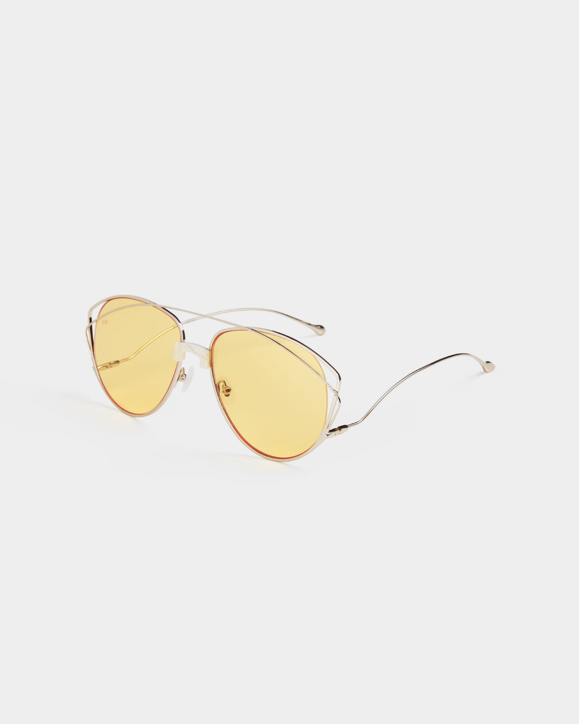 A pair of aviator-style sunglasses with slender stainless steel frames and amber-tinted nylon lenses is shown against a white background. Boasting 100% UV protection, the arms of the For Art's Sake® Dark Eyes glasses are thin and slightly curved at the tips.