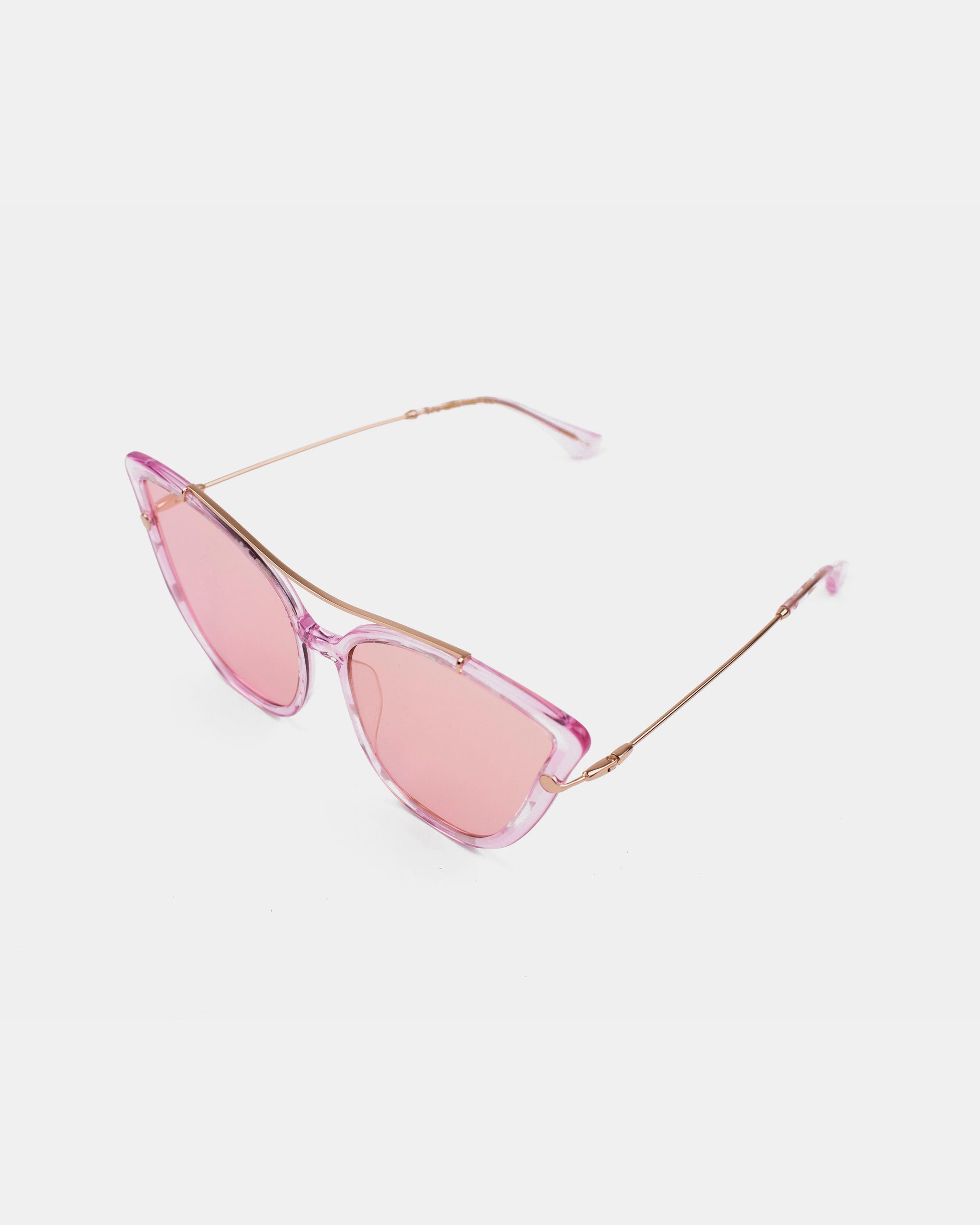 The T Two sunglasses by For Art's Sake® are a stylish pair of pink-tinted cat-eye glasses featuring thin gold arms and an acetate frame. The lenses provide 100% UV protection, seamlessly matching the pink-hued frame. The exaggerated cat-eye lens design blends retro charm with modern elegance, all showcased against a plain white background.