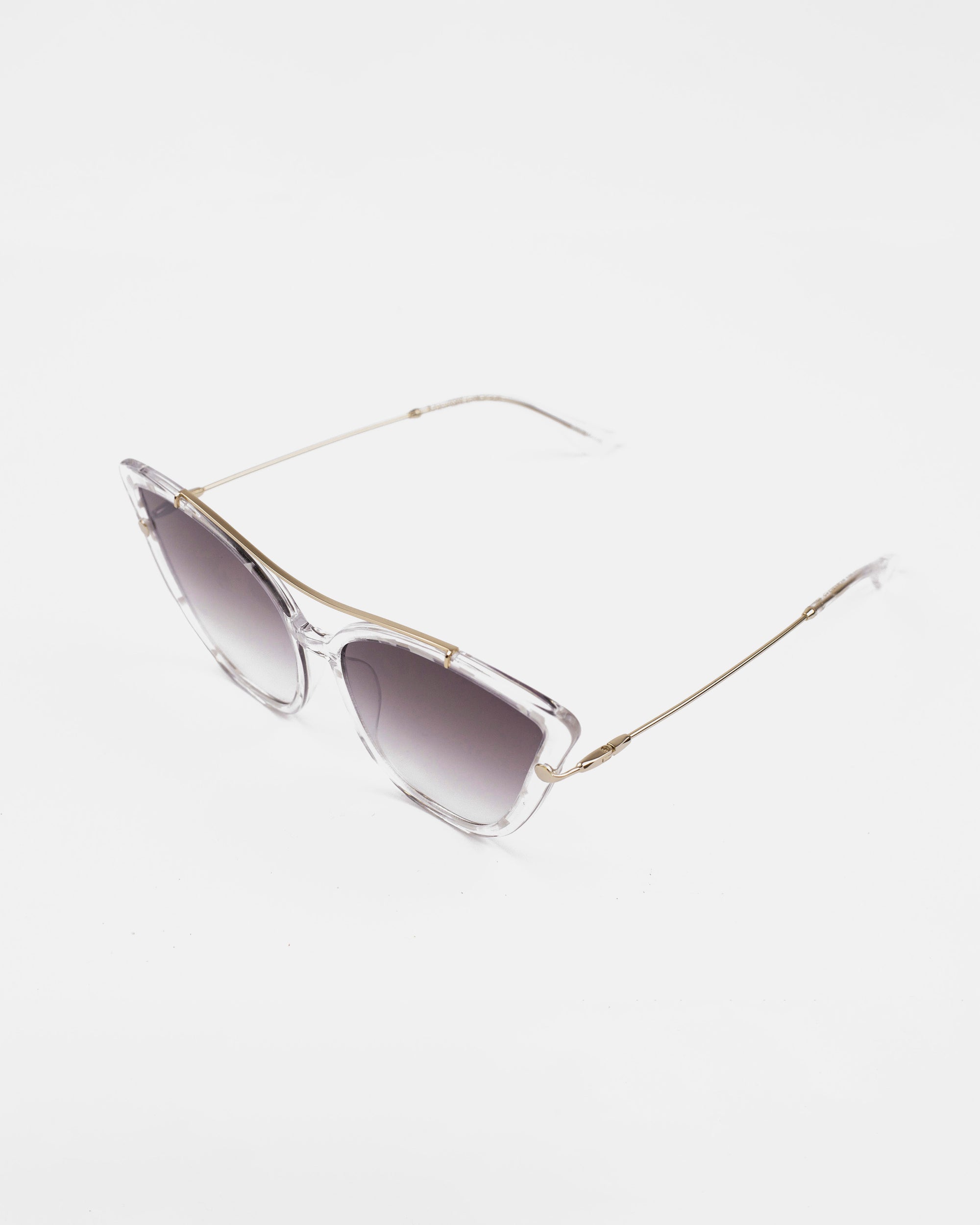 The T Two sunglasses by For Art&#39;s Sake® feature translucent, angular acetate frames paired with sleek, thin gold arms. The gradient dark lenses provide 100% UV protection while exuding a chic and modern look. These stylish glasses are elegantly displayed against a plain white background.