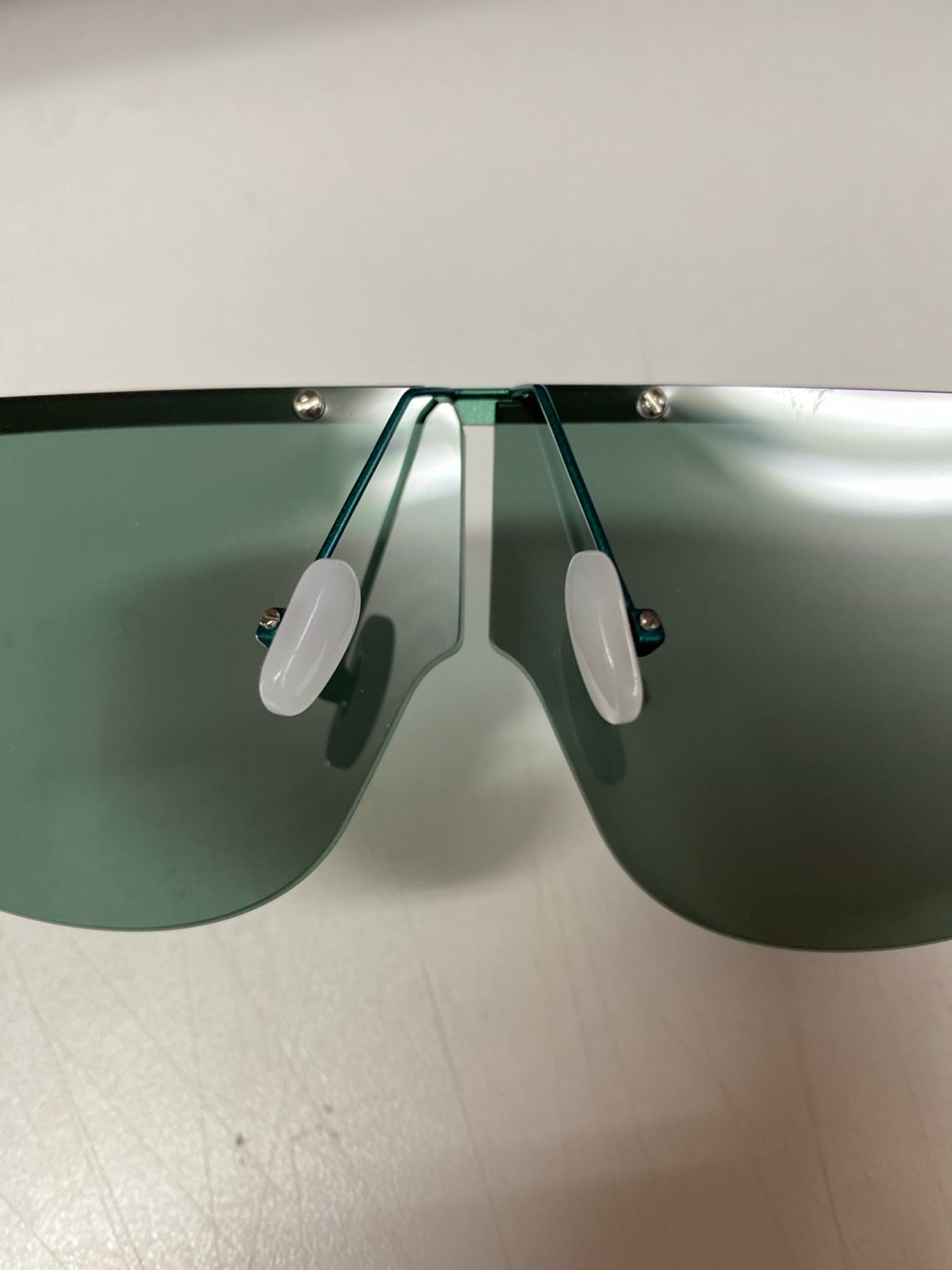 A close-up of a pair of For Art&#39;s Sake® Air sunglasses featuring oversized, dark-tinted, UV-protected lenses and nose pads. These sunglasses boast a sleek and modern design with a frameless top and metal connecting elements. The image is taken from the front, focusing on the lenses and nose bridge area.