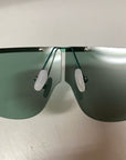 A close-up of a pair of For Art's Sake® Air sunglasses featuring oversized, dark-tinted, UV-protected lenses and nose pads. These sunglasses boast a sleek and modern design with a frameless top and metal connecting elements. The image is taken from the front, focusing on the lenses and nose bridge area.