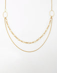 Alba Glasses Chain by For Art's Sake®: Gold necklace with three different chains: one thick oval-linked chain draped in the center and two thinner chains in varying lengths, all connected to two solid oval-shaped loops on either end. This multi-strand necklace is displayed on a plain white background.