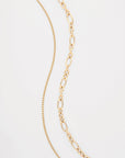 Two Alba Glasses Chains by For Art's Sake® are placed against a white background. The chain on the left, an 18K gold-plated piece, features a delicate, thin design with evenly spaced links. The chain on the right is composed of larger, oval links arranged in a slightly tapered pattern.