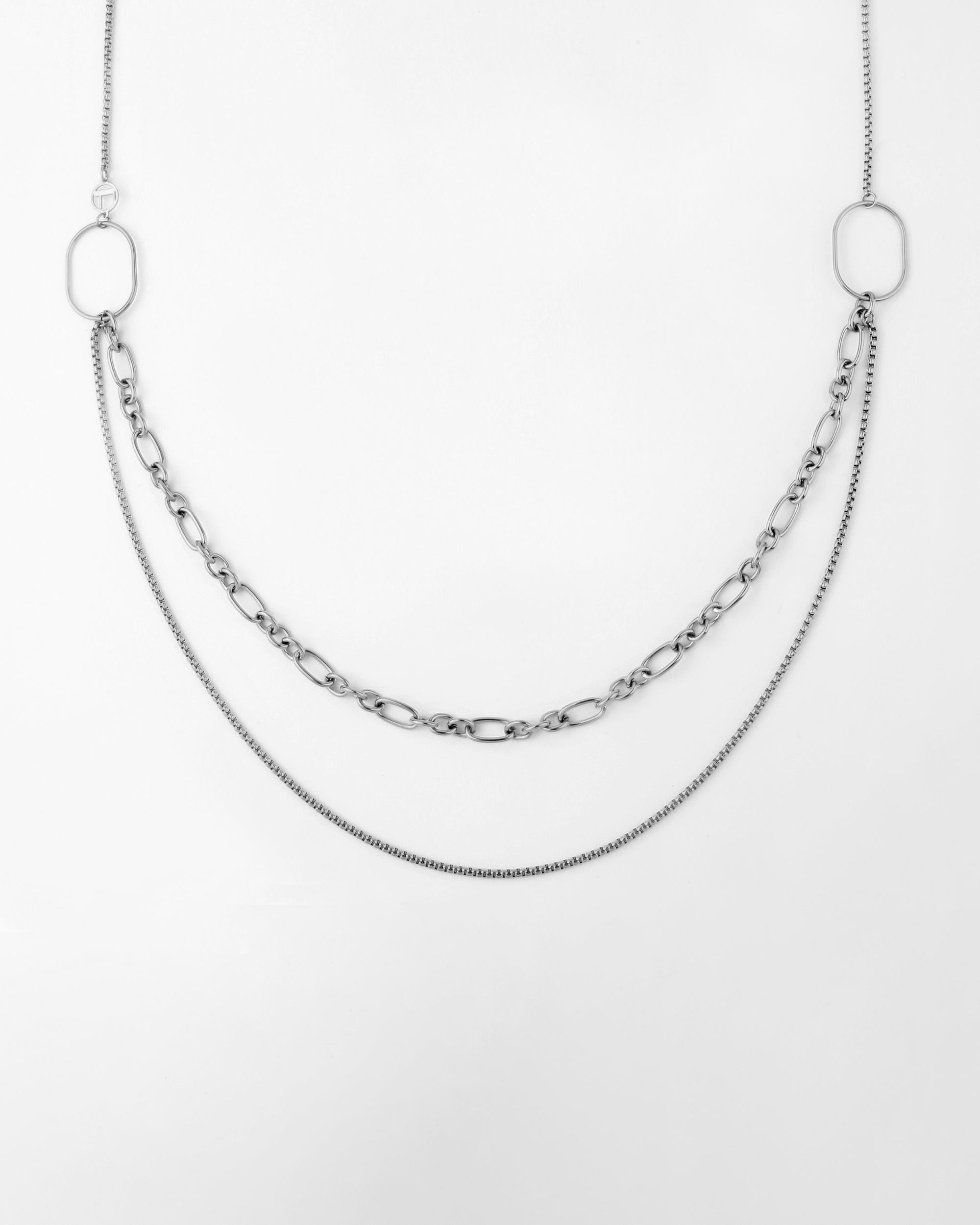 A minimalist multi-strand design necklace with two different chain styles. One chain is composed of larger oval links, while the other is a finer, thinner chain. Both chains drape in a layered manner, attached to two large oval loops at each end. The background is white. This Alba Glasses Chain by For Art's Sake® offers versatility and elegance to any accessory collection.