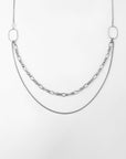 A minimalist multi-strand design necklace with two different chain styles. One chain is composed of larger oval links, while the other is a finer, thinner chain. Both chains drape in a layered manner, attached to two large oval loops at each end. The background is white. This Alba Glasses Chain by For Art's Sake® offers versatility and elegance to any accessory collection.