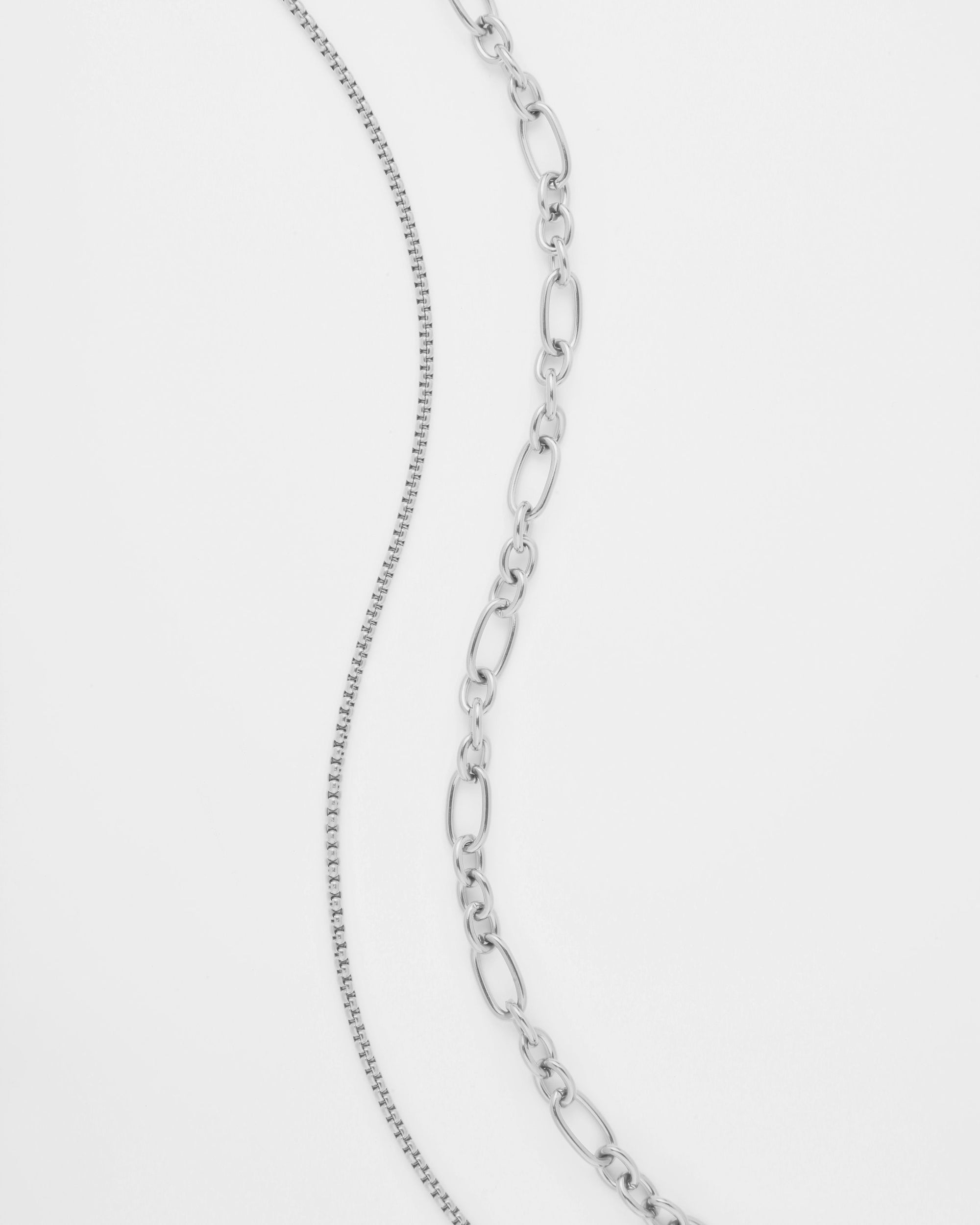 A close-up image of two silver chains set against a white background. The chain on the left has a delicate, fine link pattern, while the chain on the right features larger, oval-shaped links. Both chains, part of an elegant multi-strand necklace by For Art's Sake®, exhibit a shiny, polished finish and are known as the Alba Glasses Chain.