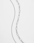 A close-up image of two silver chains set against a white background. The chain on the left has a delicate, fine link pattern, while the chain on the right features larger, oval-shaped links. Both chains, part of an elegant multi-strand necklace by For Art's Sake®, exhibit a shiny, polished finish and are known as the Alba Glasses Chain.