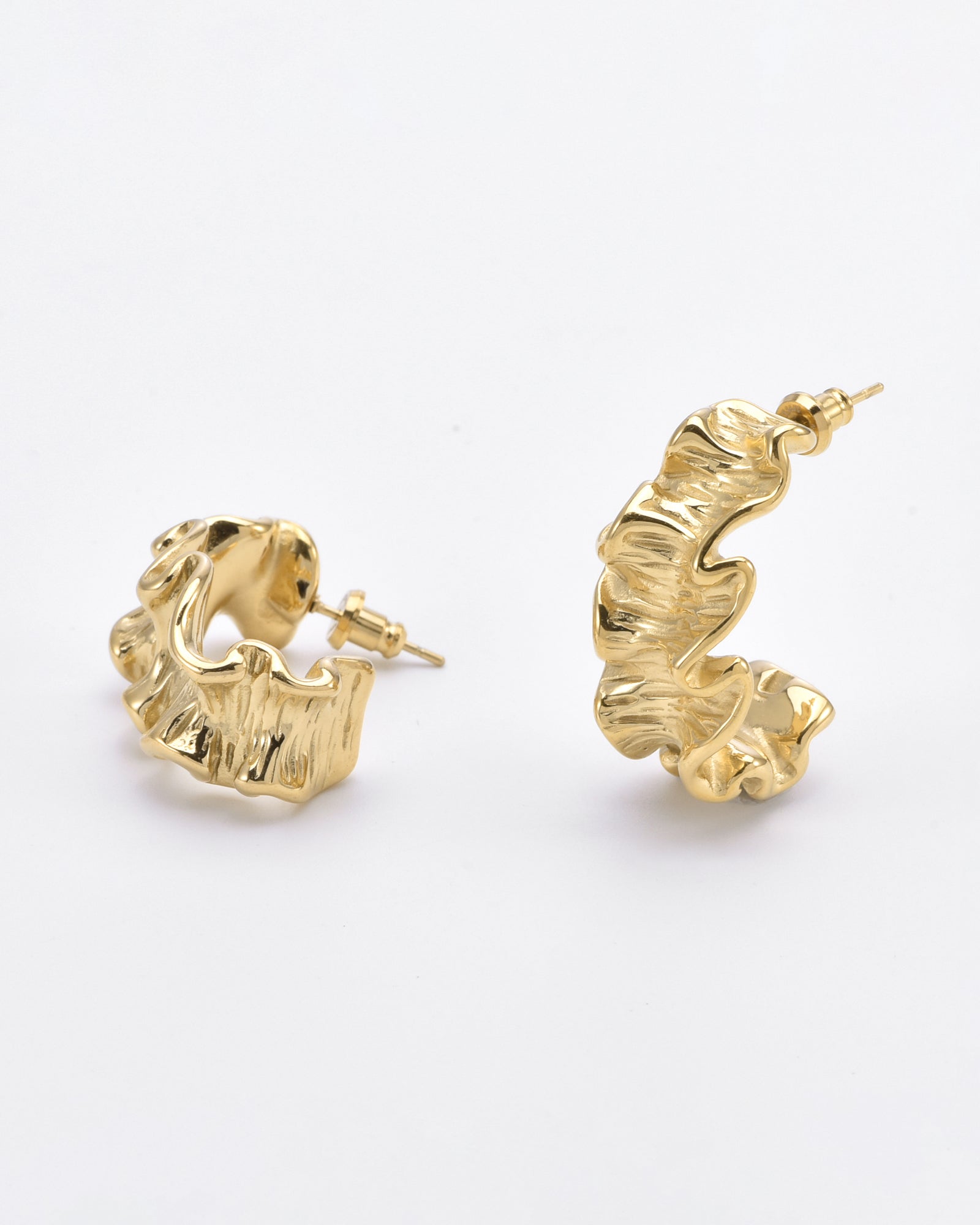A pair of For Art's Sake® Athena Earrings Gold with a ribbon-inspired silhouette features a unique, textured, ruffled design. One earring is lying flat while the other is standing upright, both resting on a plain white surface, showcasing their elegant design in 24k gold.