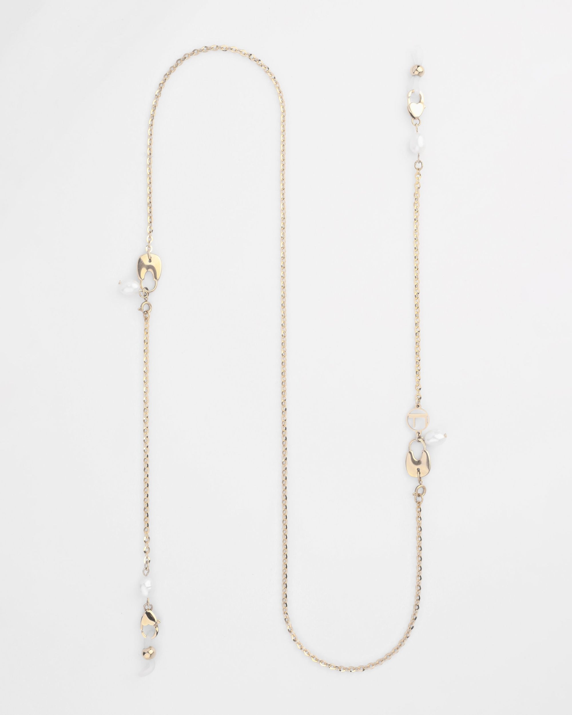 A delicate For Art's Sake® Belgravia Glasses Chain with various small adornments, including freshwater pearl drops and uniquely shaped gold pieces, laid out on a plain white background. The chain features irregular intervals of decorative elements, adding an elegant and intricate design.