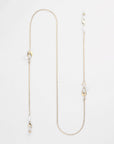 A delicate For Art's Sake® Belgravia Glasses Chain with various small adornments, including freshwater pearl drops and uniquely shaped gold pieces, laid out on a plain white background. The chain features irregular intervals of decorative elements, adding an elegant and intricate design.