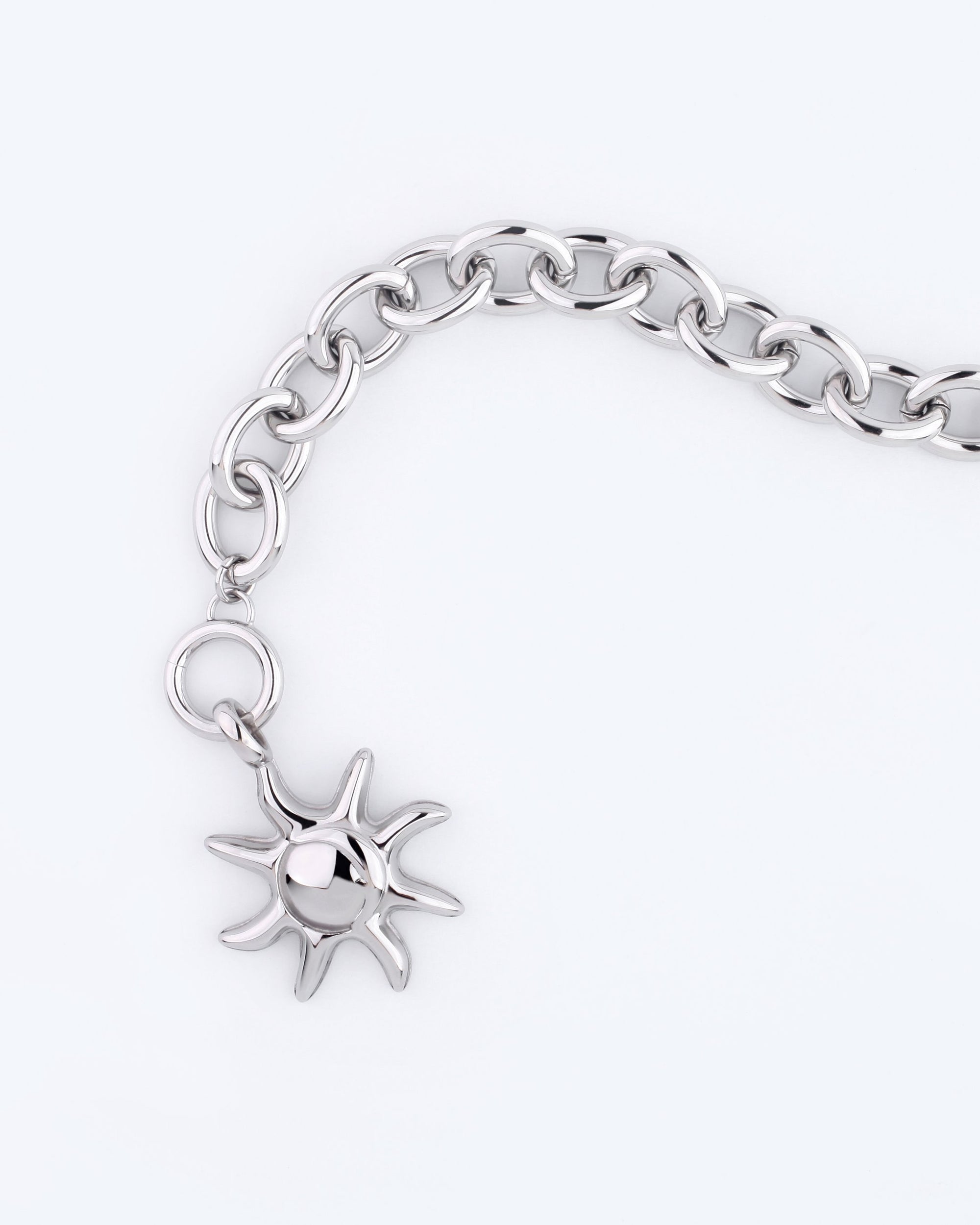 A bracelet from For Art&#39;s Sake® showcases a sun charm, set on a light background, featuring an ornamental chain design.