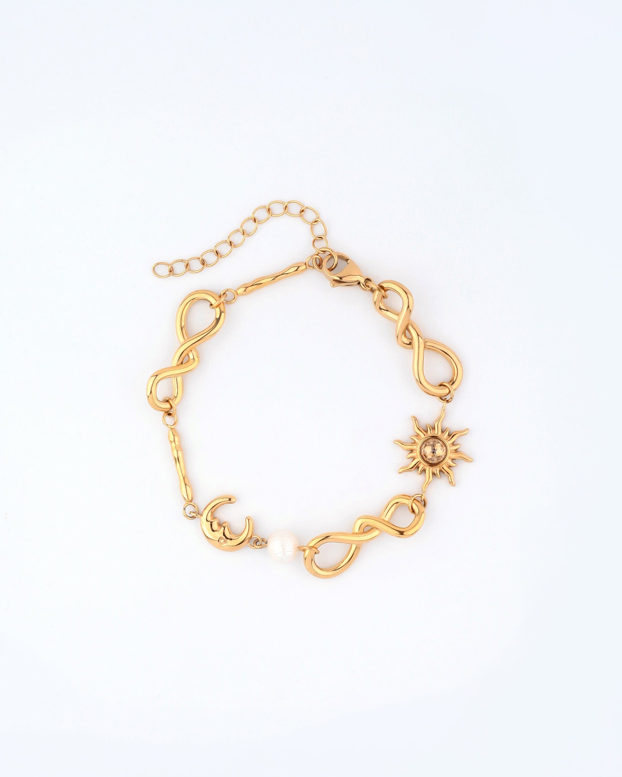 The Sloane Bracelet by For Art&#39;s Sake® is a gold bracelet showcasing an infinity link chain, embellished with a crescent moon charm, a round bead, and a sun charm with pointed rays. It features an adjustable extension chain for the perfect fit and secures with a lobster clasp.