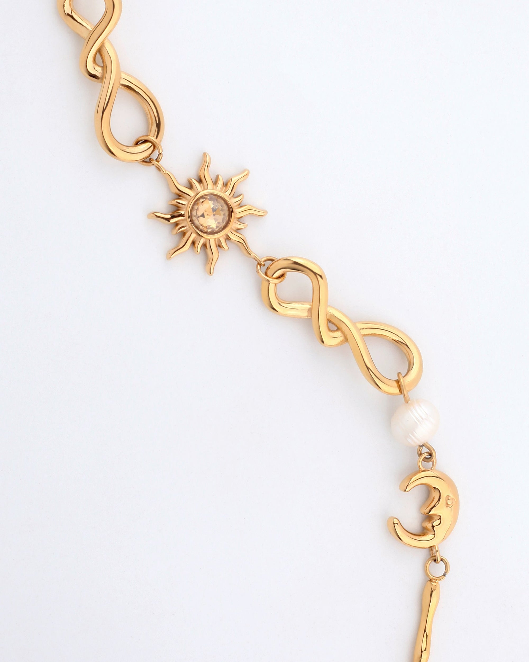 The Sloane Bracelet by For Art&#39;s Sake® showcases an intertwined infinity symbol adorned with a sun charm featuring a crystal center, complemented by a white pearl and a crescent moon charm. This elegant bracelet boasts a celestial-themed design and includes an adjustable length for the ideal fit.