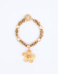 The Blossom Bracelet from For Art's Sake® is a gold chain bracelet with intricate links, highlighted by a large flower pendant. It elegantly wraps around the wrist and features a toggle clasp, lying gracefully on a plain light background.