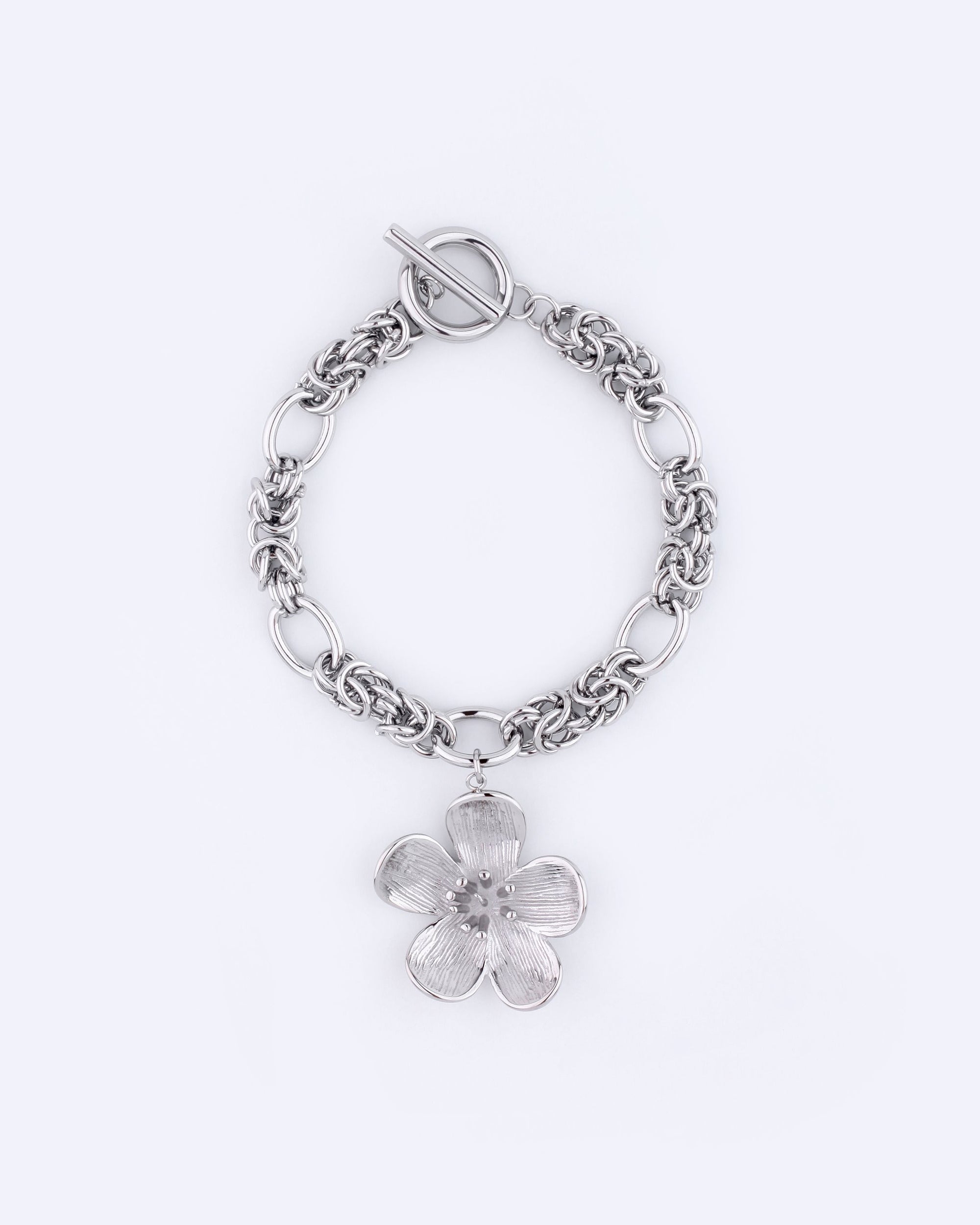 Introducing the &quot;Blossom Bracelet&quot; by For Art&#39;s Sake®, a stunning silver chain bracelet featuring a toggle clasp and a prominent flower charm. This elegant piece measures 20.5cm in length, with the flower displaying five intricately detailed petals, beautifully highlighted against a plain white background.