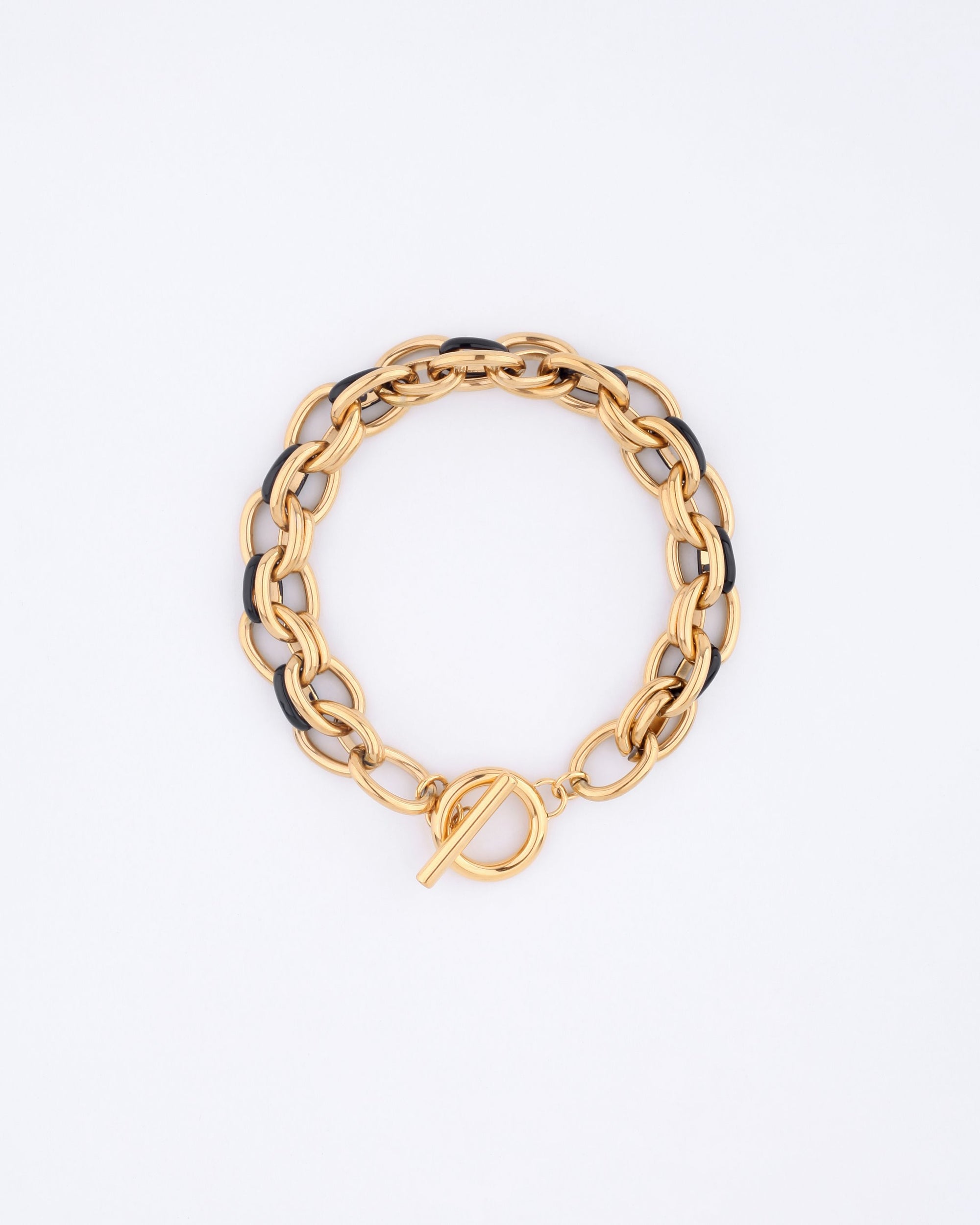 The Raya Bracelet by For Art&#39;s Sake® is a gold chain bracelet, measuring 20.5cm in length, with alternating black and gold links and a toggle clasp, elegantly displayed in a circular shape on a white background.