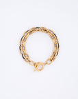 The Raya Bracelet by For Art's Sake® is a gold chain bracelet, measuring 20.5cm in length, with alternating black and gold links and a toggle clasp, elegantly displayed in a circular shape on a white background.