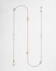 A Brixton Glasses Chain with a delicate, 18kt gold-plated chain featuring various charms including stars, moons, small round beads, and a freshwater pearl. The charms are spaced evenly, adding an elegant touch to the simple chain. The chain is laid out flat on a white background. This exquisite piece is crafted by For Art's Sake®.