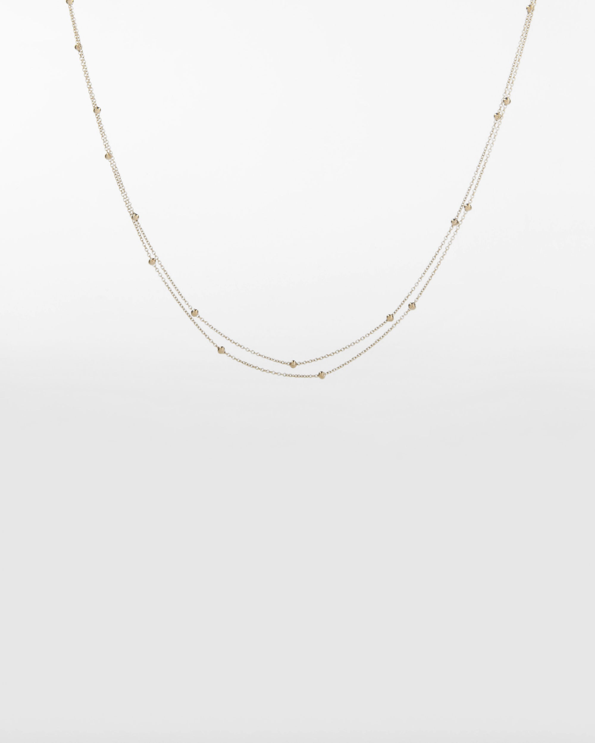 A minimalist, double-layered 18kt gold-plated necklace with small, evenly spaced beads along the chains. The background is plain and light, highlighting the delicate design and multi-strand elegance of this piece—Beetle Glasses Chain by For Art's Sake®.