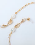 The For Art's Sake® Buddha Glasses Chain is a delicate 18-karat gold-plated chain necklace with two small hands clasping parts of the chain, each holding a white freshwater pearl. The chain features elongated links, and the hands serve as unique decorative elements. One end of the chain has a round gold bead.