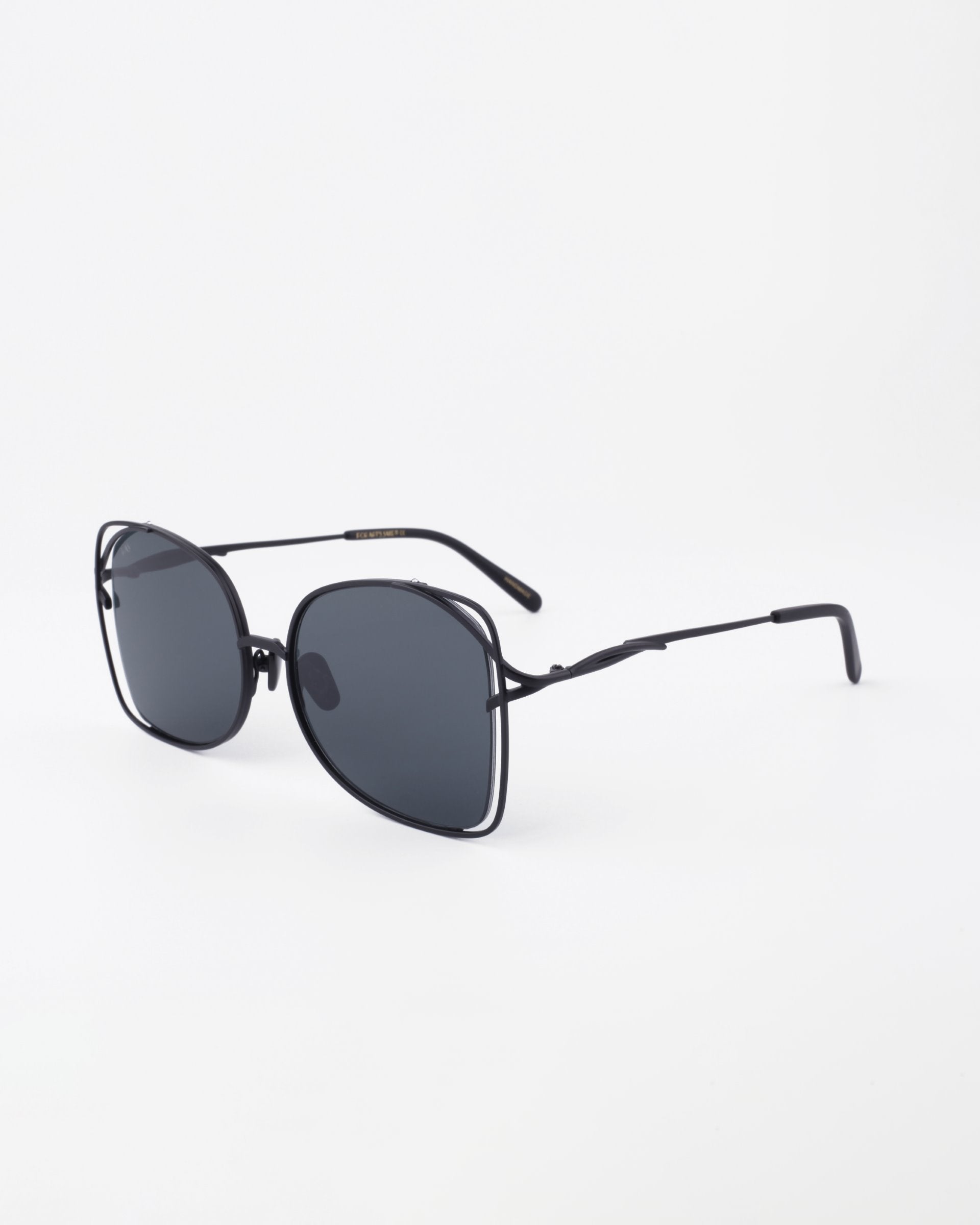 A pair of sleek, oversized handmade Carousel sunglasses by For Art&#39;s Sake® with dark lenses and a thin black metal frame. The sunglasses are angled slightly to the right and placed on a plain white background, offering both UVA &amp; UVB protection.