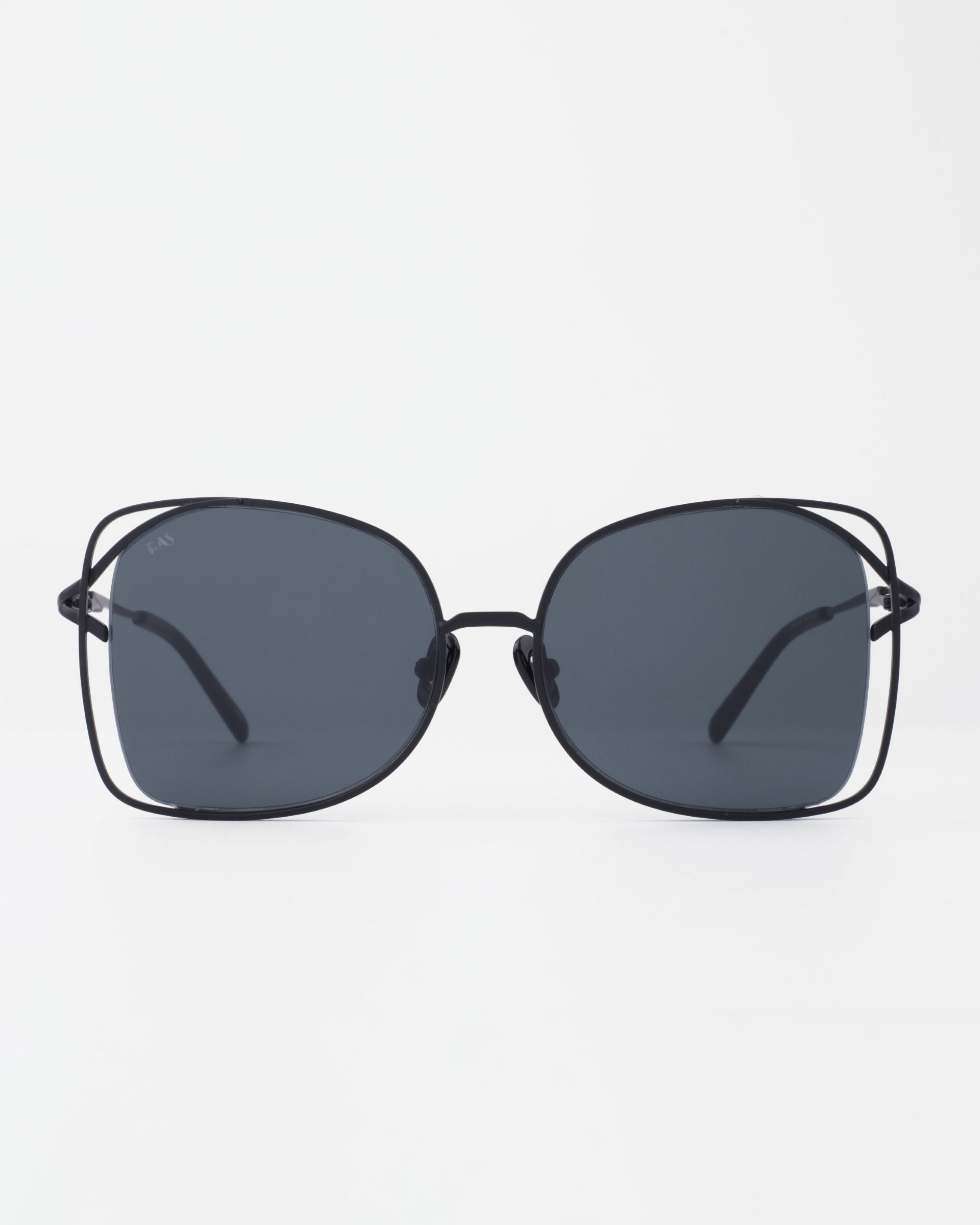 A pair of black-framed Carousel sunglasses by For Art&#39;s Sake® with large, slightly rounded square lenses and thin temples. The lenses are dark tinted, providing a sleek and stylish appearance with UVA &amp; UVB protection. Handmade sunglasses crafted for elegance. The background is plain white.
