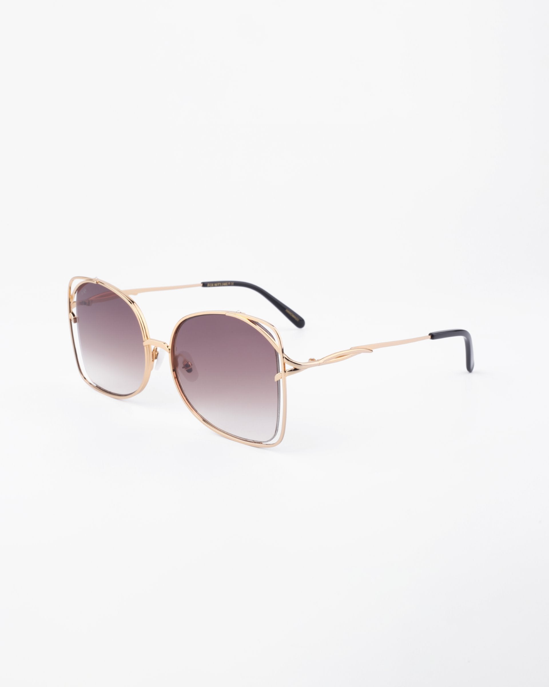A pair of stylish, handmade sunglasses with large, square-shaped lenses shaded from dark to light. The Carousel sunglasses by For Art's Sake® feature a thin, gold-plated stainless steel frame with black temple tips. They offer complete UVA & UVB protection. The background is plain white.