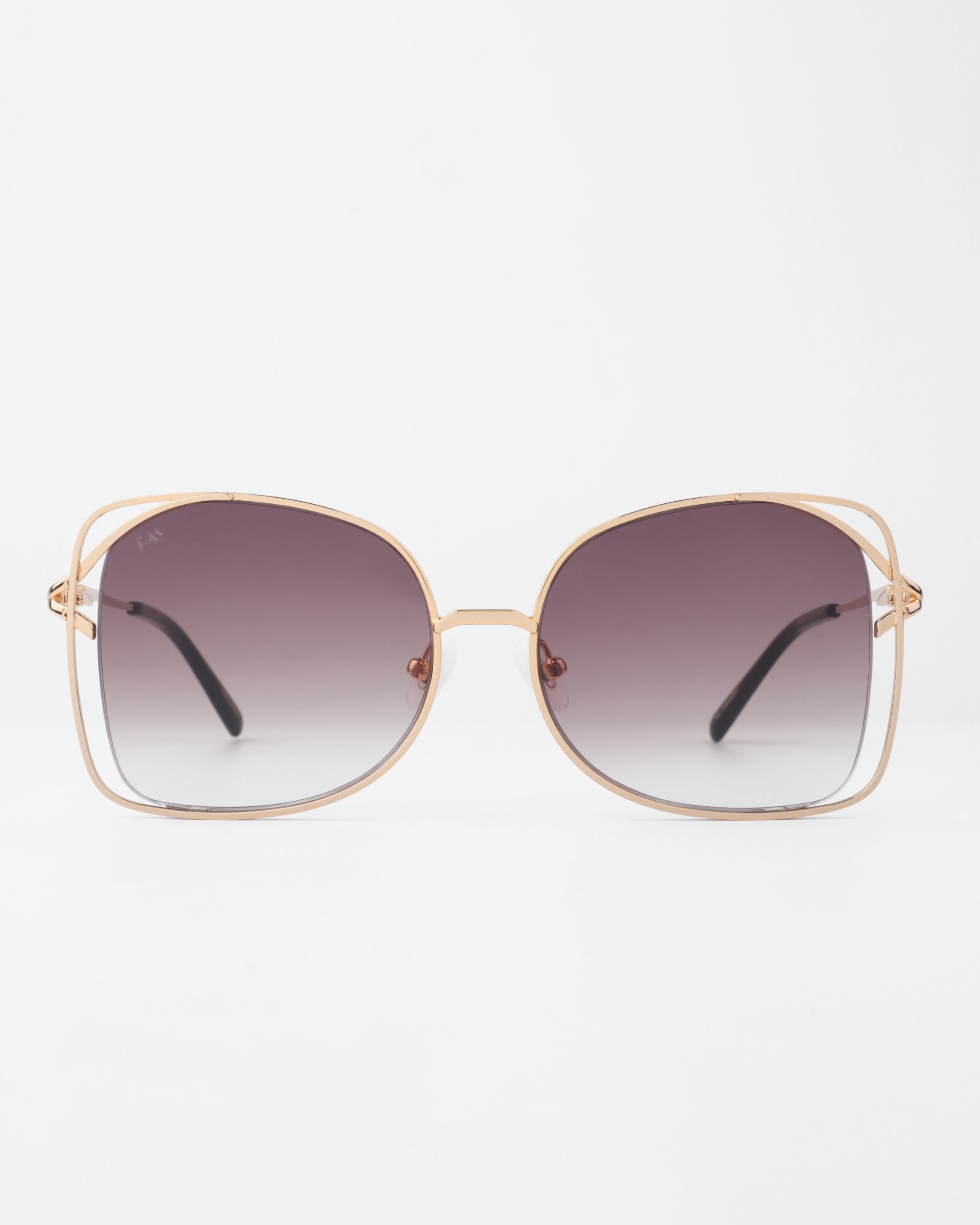 A pair of large, square handmade Carousel sunglasses from For Art&#39;s Sake® with gold-plated stainless steel frames and gradient lenses, transitioning from dark at the top to lighter at the bottom. The sunglasses offer UVA &amp; UVB protection and are placed upright against a white background.