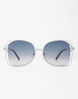 A pair of oversized, handmade Carousel sunglasses from For Art's Sake® with rounded square frames made of thin silver metal. The gradient lenses transition from dark blue at the top to clear at the bottom, providing UVA & UVB protection. The sunglasses feature thin arms with black tips. The background is plain white.