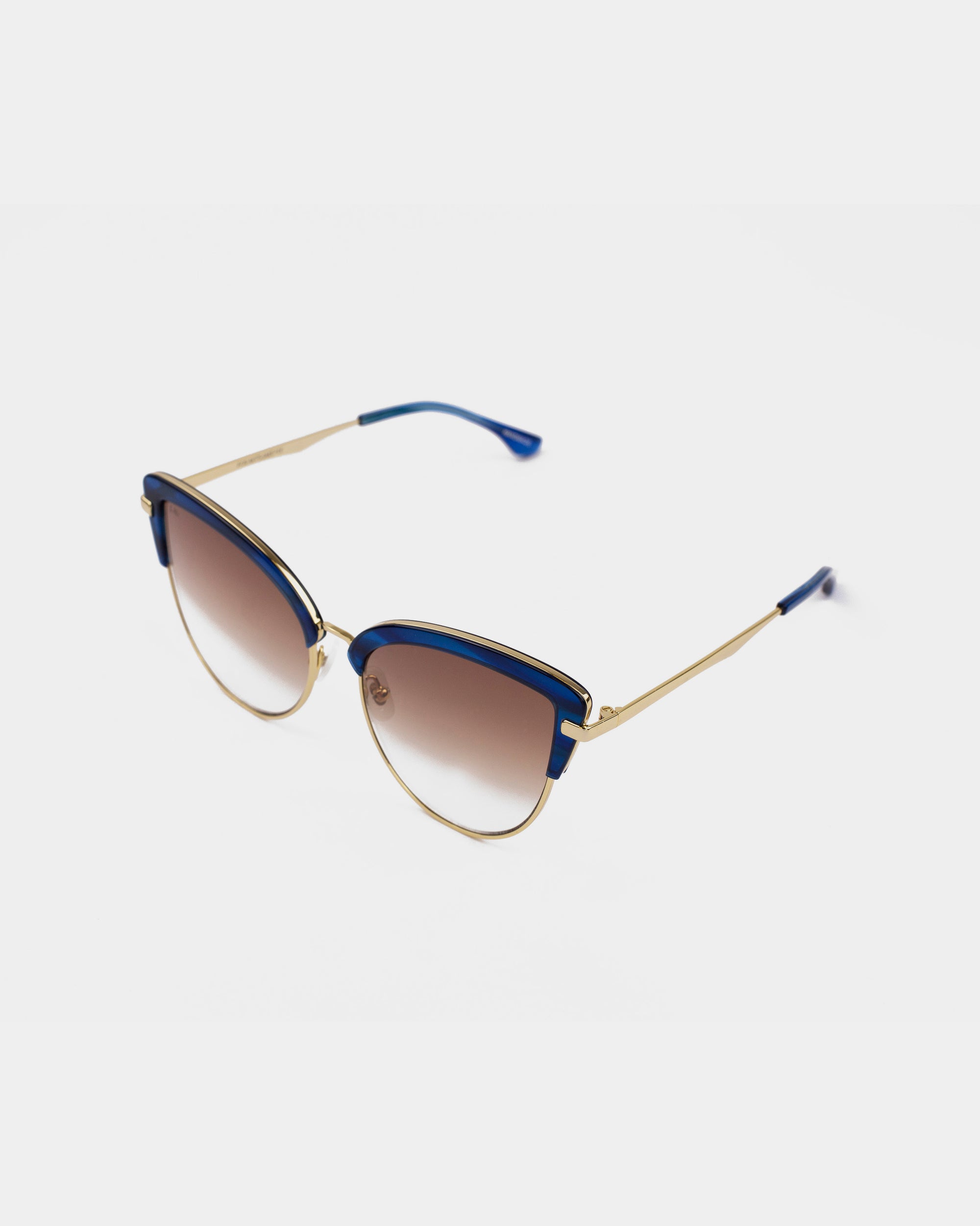 A pair of stylish Venus sunglasses by For Art&#39;s Sake® featuring stainless steel frames with 18-karat gold plating, blue accents along the top edge, and gradient brown nylon lenses. The temple arms are gold with blue tips, giving the eyewear a fashionable and elegant look.