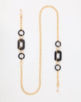 A stunning 18-karat gold-plated chain with black geometric accents is shown against a white background. The NYC Glasses Chain by For Art's Sake®, featuring oversized acetate links in rectangular and circular shapes, exudes NYC chain chicness throughout its length.