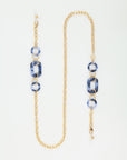 A stylish NYC Glasses Chain composed of an 18-karat gold-plated chain interspersed with blue marbled resin rings and rectangular links by For Art's Sake®. The design alternates between the resin pieces and gold chain, creating a balanced and elegant look against a white background.