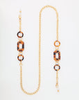 18-karat gold-plated eyeglass chain with oversized acetate links and interspersed brown tortoise shell-like rings. The For Art's Sake® NYC Glasses Chain features a lobster clasp at one end and adjustable loops at the other for attaching to glasses. The overall appearance is stylish and functional.
