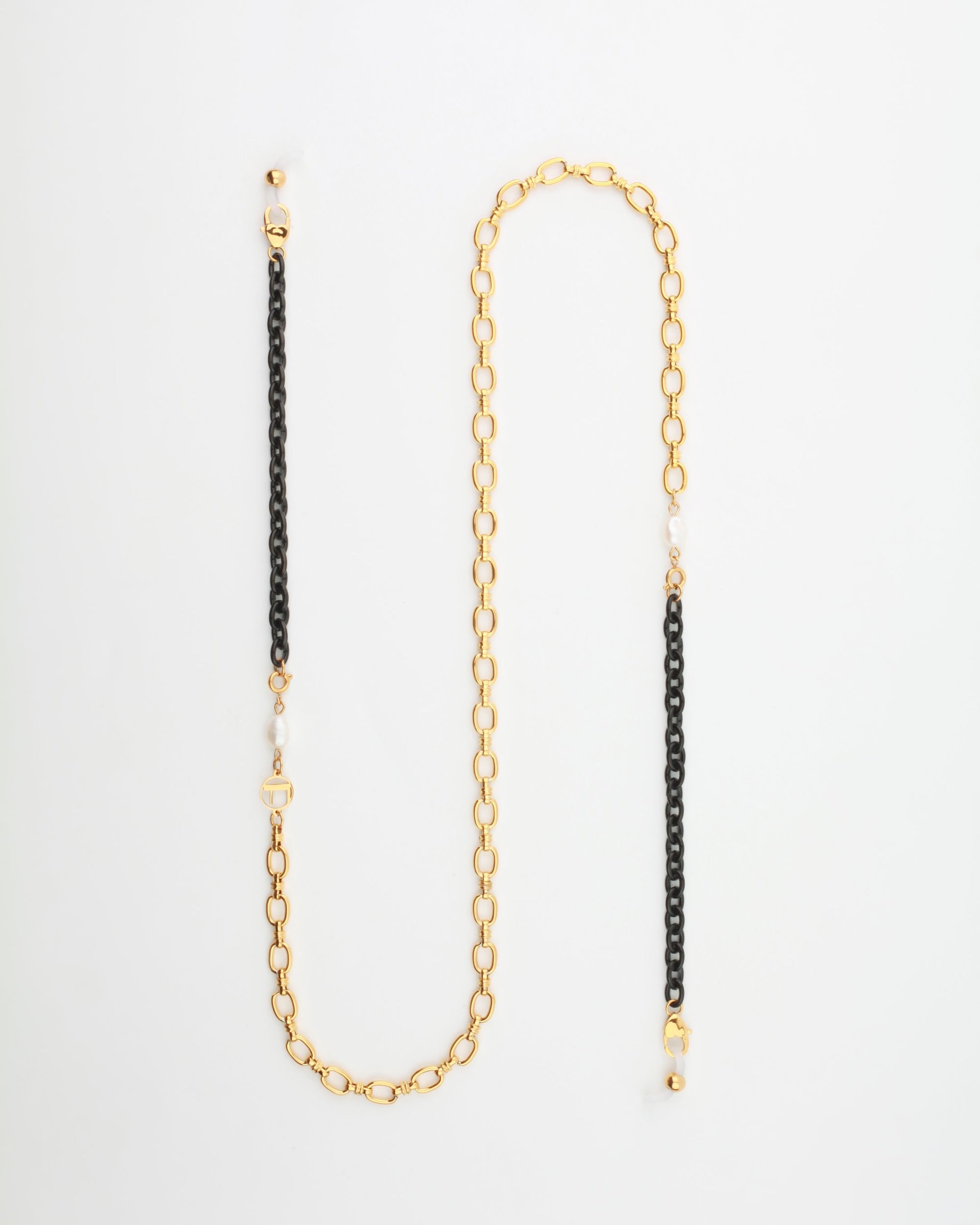 A stylish 18-karat gold-plated eyewear chain with alternating sections of gold and black links. The gold links are elegantly large and oval, while the black links are smaller and round. Freshwater pearls are interspersed along the chain, adding a touch of sophistication. Introducing the Tokyo Glasses Chain by For Art's Sake®.