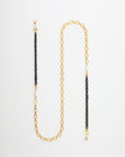 A stylish 18-karat gold-plated eyewear chain with alternating sections of gold and black links. The gold links are elegantly large and oval, while the black links are smaller and round. Freshwater pearls are interspersed along the chain, adding a touch of sophistication. Introducing the Tokyo Glasses Chain by For Art's Sake®.